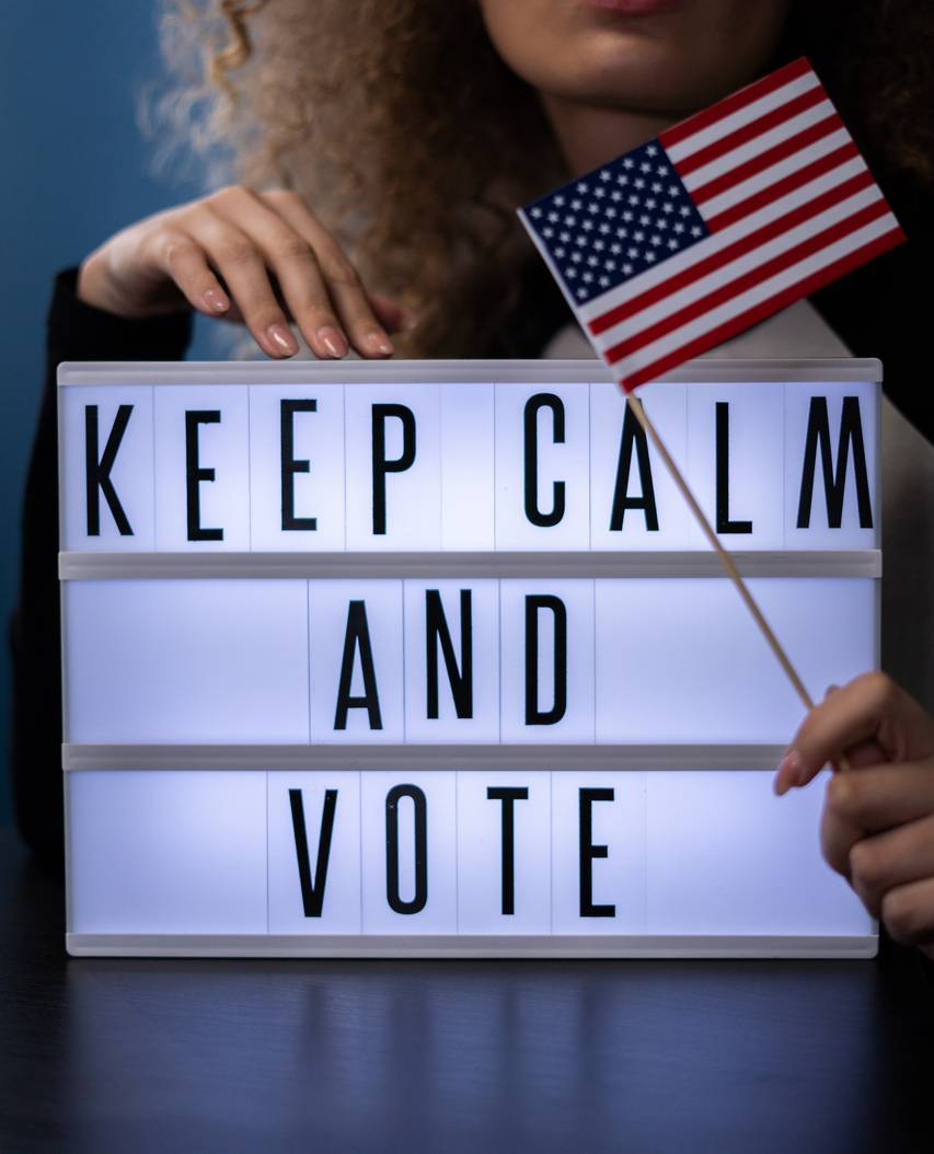 woman behind a sign and holding an american flag